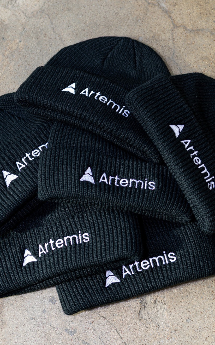 Stack of black ribbed beanies with white embroidered Artemis logos