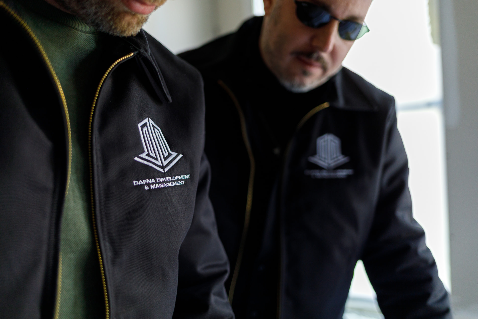 Two men wearing black work jackets with white embroidered Dafna Development & Management logos